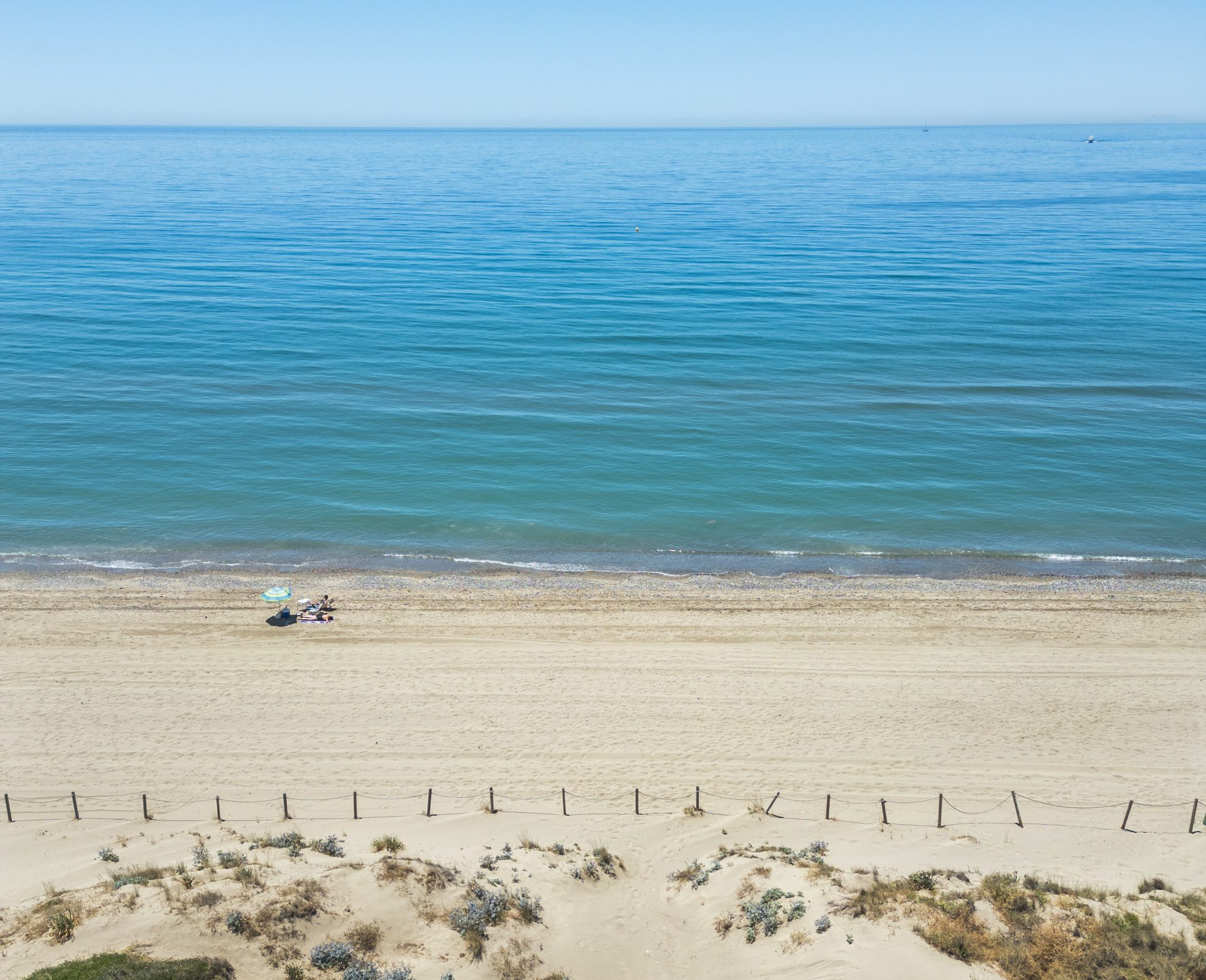 The open sea, the shoreline, the width of the beach and the fenced protected dune in front of Bahía de Marbella