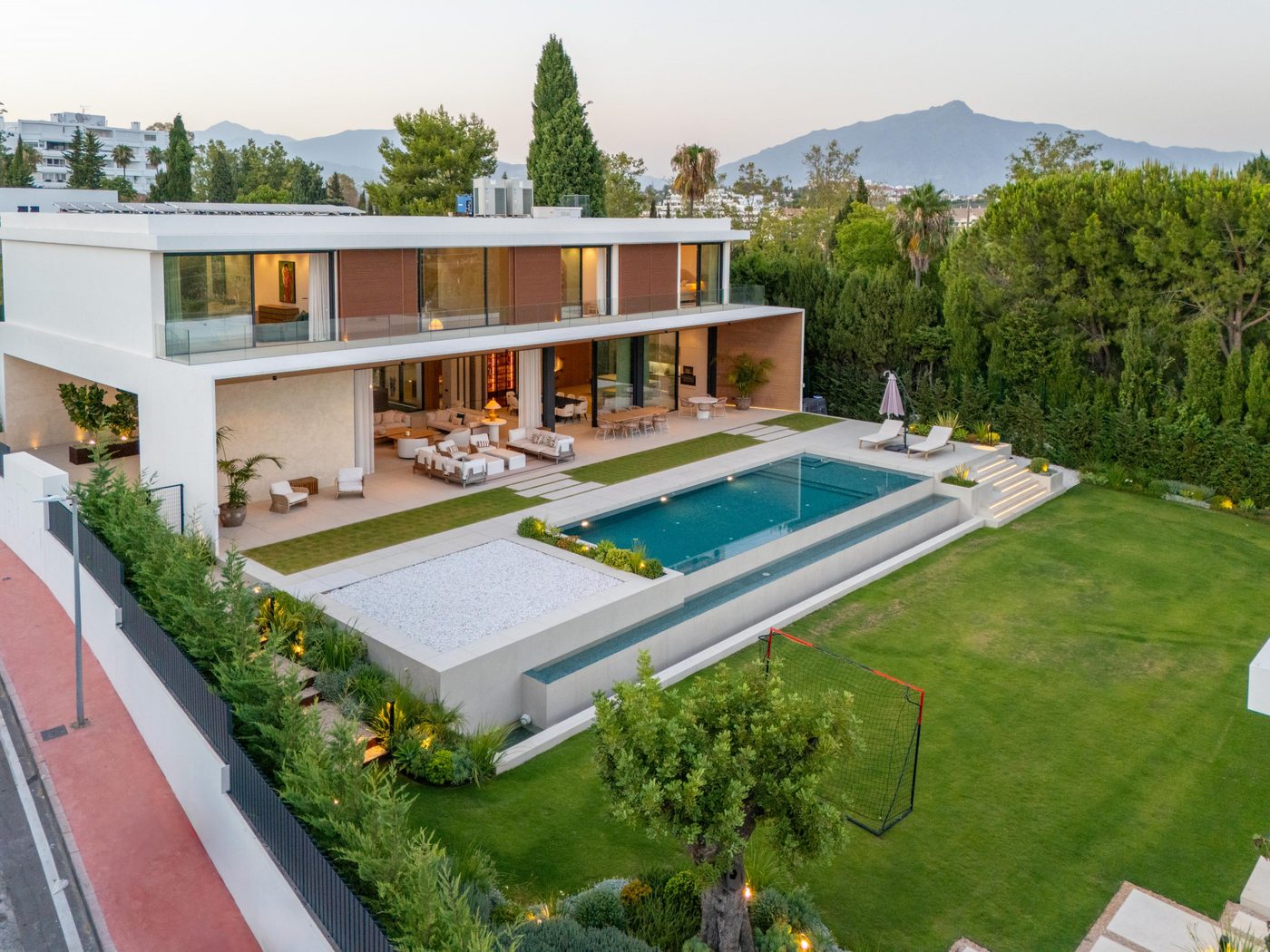 A villa in Guadalmina Alta at dusk, its pool and lawn, with the sierra behind