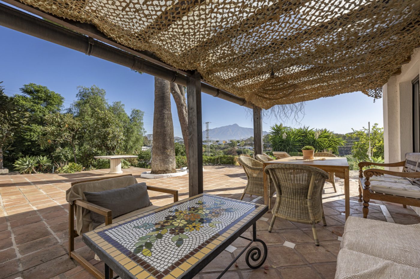 A shaded terrace in Guadalmina Alta under an esparto canopy, looking inland to the mountains