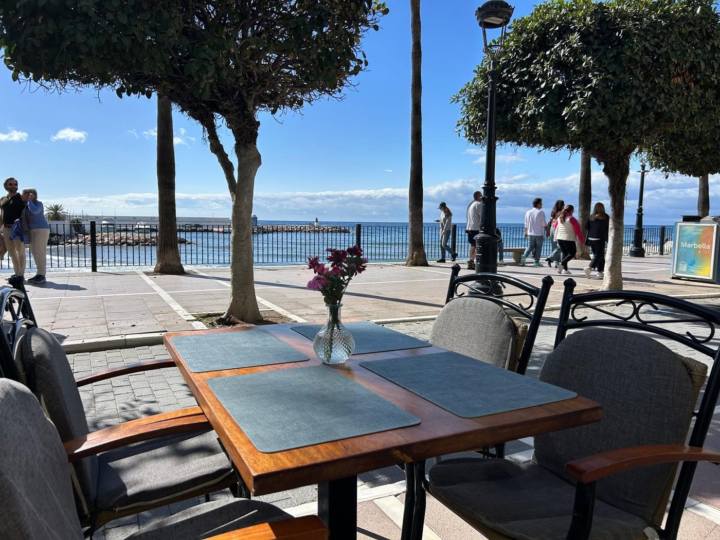 A café table on the Paseo Marítimo in Marbella with people walking past on the promenade