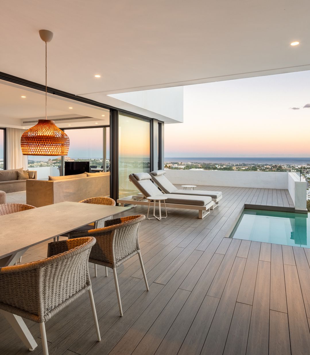 Marbella villa terrace at dusk with an infinity pool and dining table looking out over the coast towards the sea