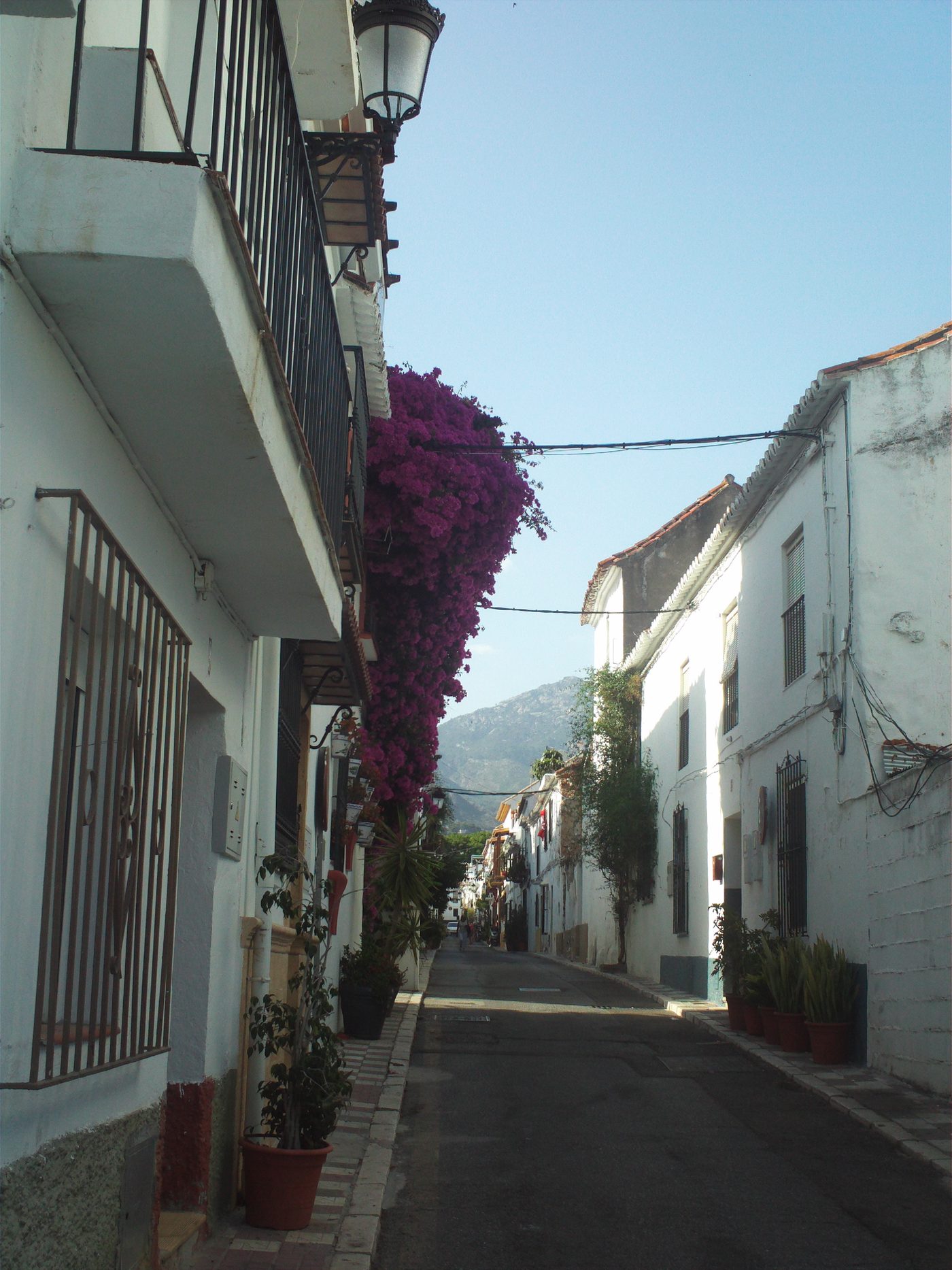 A quiet residential lane in Marbella Old Town, bougainvillea over the street and the sierra at the end of it