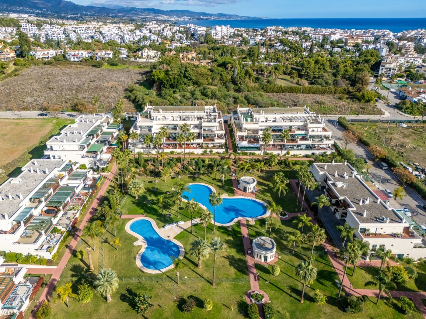 Rooftops and gardens of Nueva Andalucía from the air, with the sea beyond