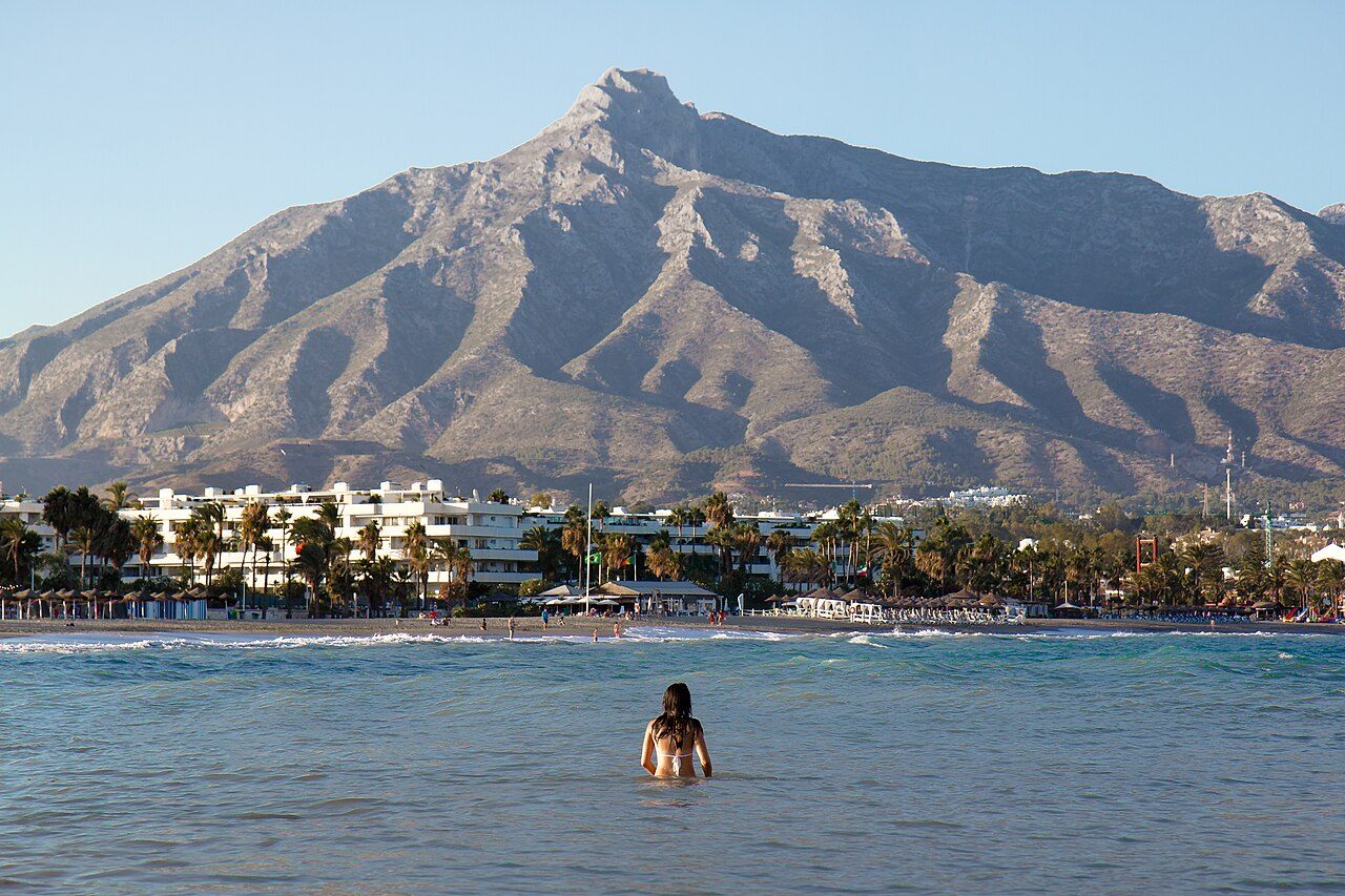 A swimmer in the sea off a Marbella beach, with the Sierra Blanca mountain behind