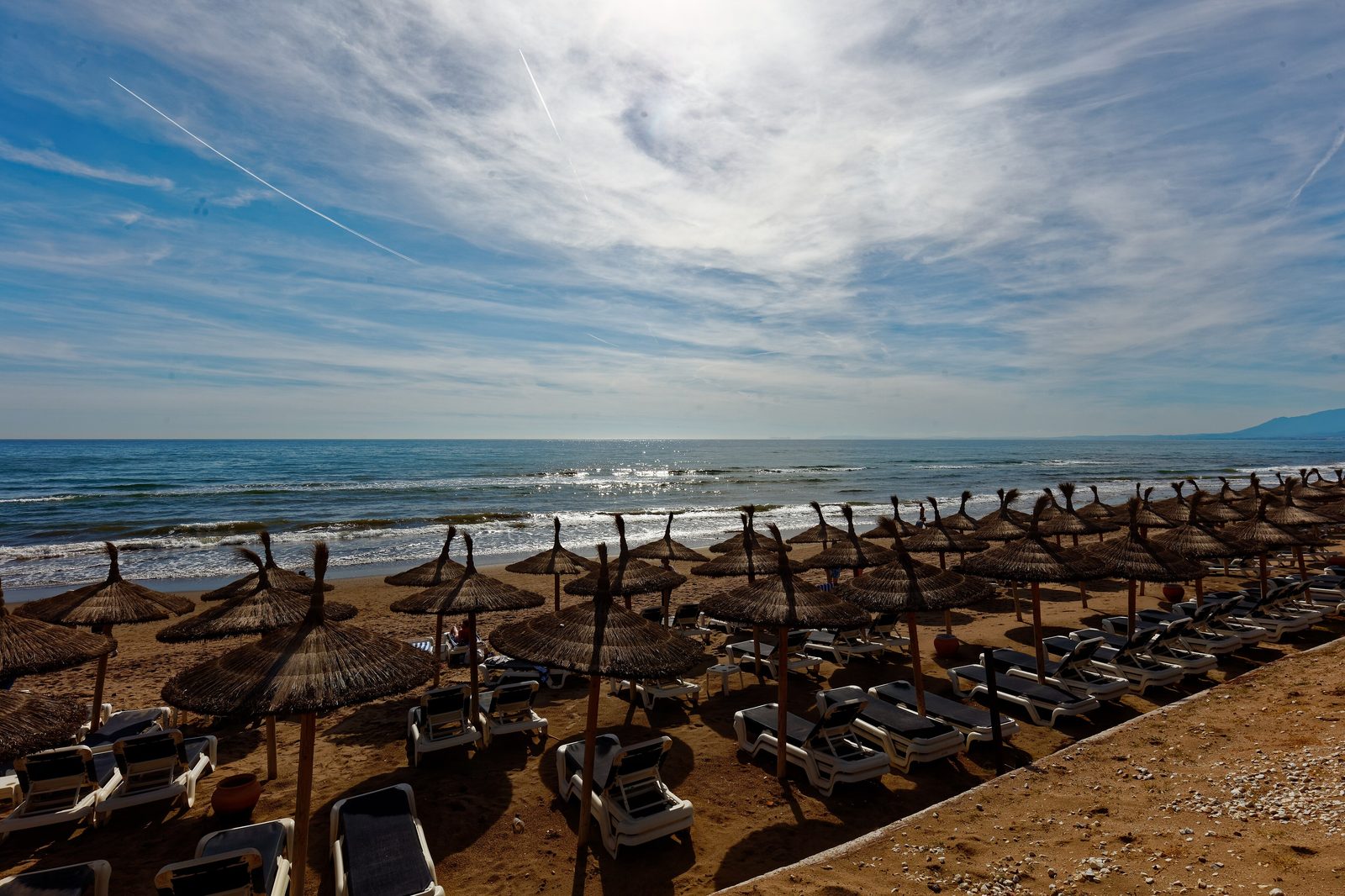 A Marbella beach with palm parasols under an autumn sky